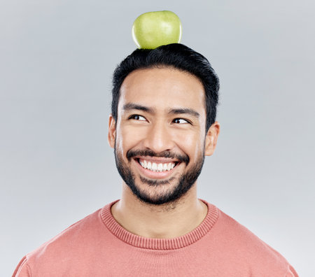Happy, healthy and an Asian man thinking of an apple isolated on a white background in a studio. Smile, idea and a Chinese guy with a fruit for nutrition, diet and organic wellness on a backdropの写真素材