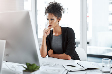 Focus from start to finalisation. a young businesswoman using a computer at her desk in a modern office.の写真素材