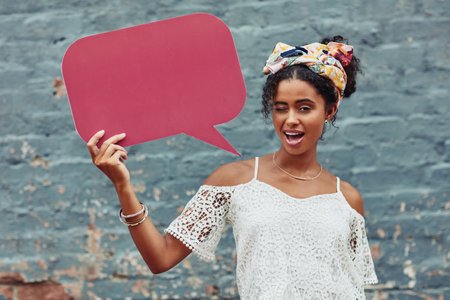 My message for you is be yourself. an attractive young woman holding a speech bubble against a brick wall outside.の写真素材