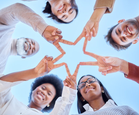 Star, low angle or happy team with peace sign, diversity or community collaboration with blue sky. Portrait, smile or group of people smiling with support, solidarity or motivation together outdoorsの写真素材