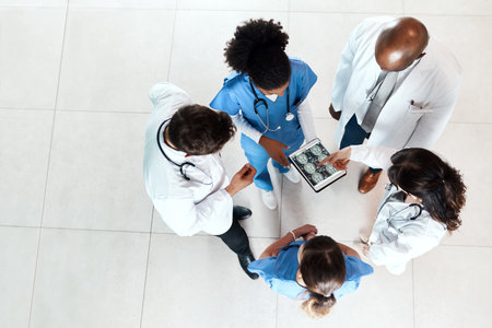 Working together like a well oiled medical machine. High angle shot of a team of doctors using a digital tablet to discuss an x ray in a hospital.の写真素材