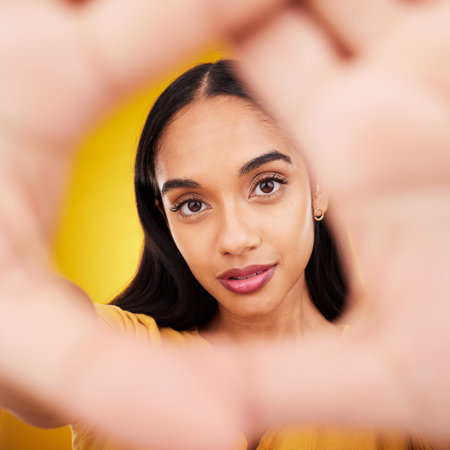 Hands, gesture and portrait of a beautiful woman isolated on a yellow background in a studio. Looking, perspective and the face of a girl in a hand frame for creativity, look through and focusの写真素材