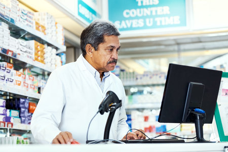 Ensuring his online systems are all operating in order. a mature pharmacist working on a computer in a chemist.の写真素材