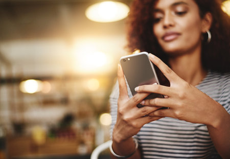 Join in on the conversation. Closeup shot of a young woman using a cellphone in a cafe.の写真素材