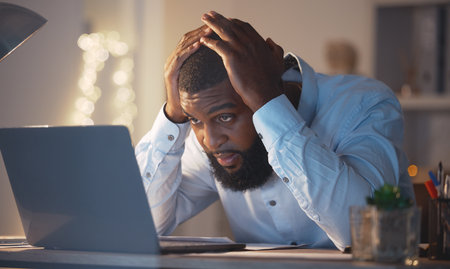 Stress, worry and black man on laptop at night working late on project deadline, online glitch and problem. Burnout, business and male worker with worried, frustrated and stressed face on computerの写真素材