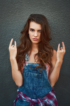Shes ready to go out rocking. Portrait of an attractive young woman holding up her hands and showing a hand sign while standing against a grey background.の写真素材
