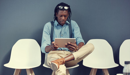 There should be an app to help with interviews. a young businessman using a tablet while waiting for an interview.の写真素材