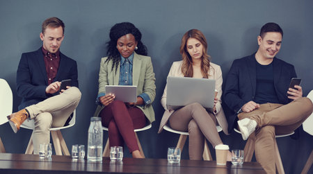The potential candidates are connected. a group of businesspeople using different wireless devices while waiting in line for an interview.の写真素材