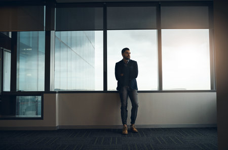You are in control of your thinking. a young businessman leaning against a wall and looking thoughtful in a modern office.の写真素材