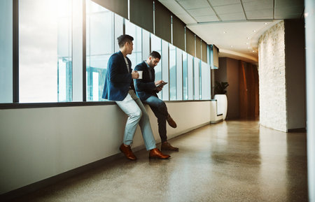 Monitoring business even on a break. a young businessman using a digital tablet while his colleague has his coffee break at work.の写真素材
