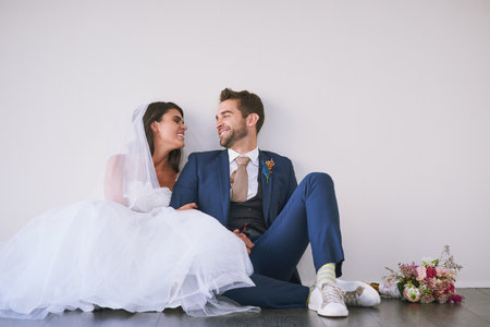 Love reigned from the first date to the I dos. Studio shot of a newly married young couple sitting together on the floor against a gray background.の写真素材