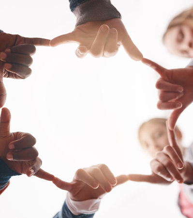 Friends for life. Low angle shot of a group of cheerful elementary school kids forming a huddle with their hands and showing a hand sign.の写真素材