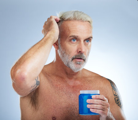 Hair care, grooming and mature man with gel isolated on a blue background in studio. Beauty, clean and a senior man with a product for styling, hairstyle and applying balm for a hairdo on a backdropの写真素材