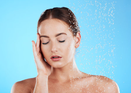 Shower, water and relax woman in a studio feeling happy from cleaning and skincare. Wellness, splash and beauty routine of a female model excited from dermatology and self care with blue backgroundの写真素材