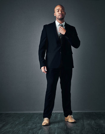 With the right suit, you can do anything. Studio shot of a handsome young businessman adjusting his tie against a gray background.の写真素材