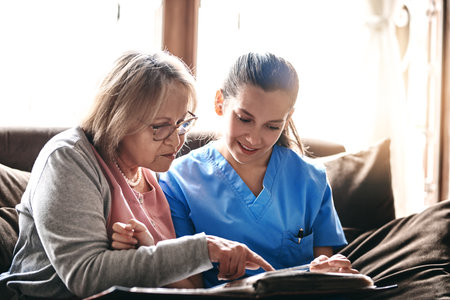 Memory exercises is very important to their health. a nurse and a senior woman looking at a photo album together.の写真素材