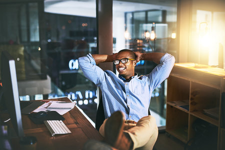 When you love what you do is it really work. a young businessman relaxing at his desk during a late night at work.の写真素材