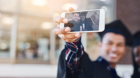 Celebrating with a selfie. two students taking a selfie on graduation day.の写真素材