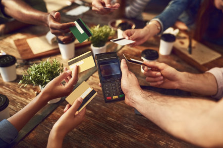 Splitting it six ways. High angle shot of an unrecognizable group of friends offering their bank cards to pay the bill at a cafe.の写真素材