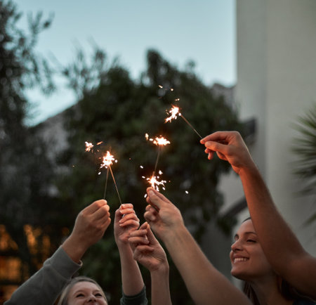 All for one and one for all. a group of cheerful young friends each holding a sparkler in the air outside.の写真素材