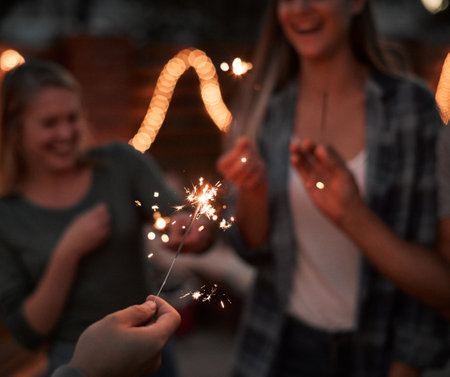 Sparkle up your life. a group of cheerful young friends having fun with sparklers together outside at night.の写真素材