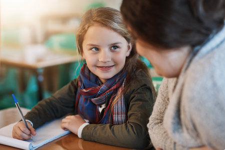 Thanks for helping me. an elementary school girl getting help from her teacher in the classroom.の写真素材