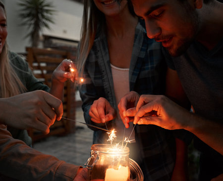 Lets light it up all at once. a group of cheerful young friends having fun with sparklers together outside at night.の写真素材