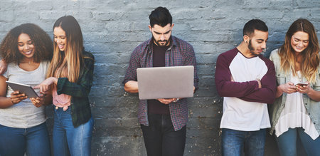 Generation connect. a group of young friends using their wireless devices together outdoors.の写真素材