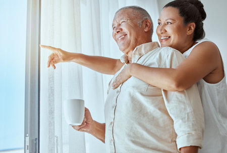 Mature couple, hug or pointing out window in house, home or retirement holiday hotel with morning coffee. Smile, happy or elderly man and love woman in show hand gesture at bonding travel hospitalityの写真素材