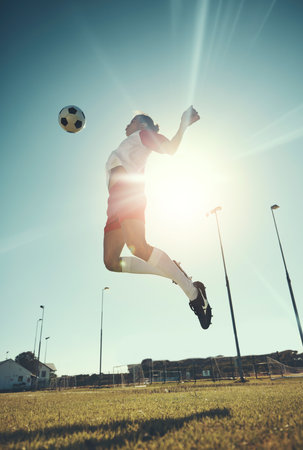 Soccer, sports and training with a man athlete jumping with a ball on a field or grass pitch for exercise. Fitness, football and workout with a male soccer player playing in a game or match outdoorの写真素材