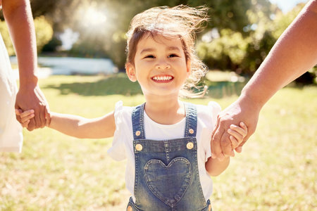 Happy, child in sun and walk with parents in nature park with a smile holding girl hands in summer sunshine. Kid in garden, smiling on grass and family relax enjoy weekend childhood outdoor freedomの写真素材