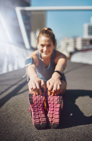 Warming up before her run. Portrait of a sporty young woman stretching before a run.の写真素材