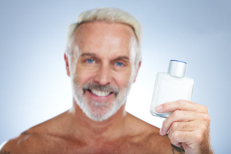 Old man, cologne aftershave and portrait in a studio with perfume and spray bottle product with a smile. Isolated, grey background and happiness of a senior and elderly model with beauty routineの写真素材