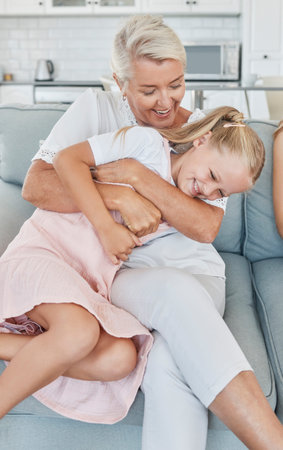 Grandmother, family and child at home with a senior woman having fun, bonding and laughing for tickle and playing on living room sofa. Grandma and girl grandchild spending time in Australia houseの写真素材