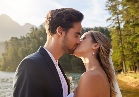 Love, wedding and kiss with a newlywed couple by a lake outdoor in celebration of marriage or romance. Water, summer and a bride and groom kissing while bonding together in tradition after ceremonyの写真素材