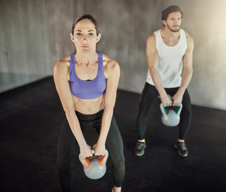 Go hard or go home. two young people working out in the gym using kettle bells.の写真素材