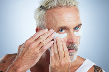 Beauty, eye mask and portrait of senior man in studio for wellness, facial treatment and anti aging cosmetics. Skincare, dermatology and face of male model with patches for detox, wrinkles and eyesの写真素材