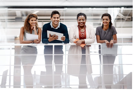 Smiling our way through our goals. a young diverse group of colleagues standing together in the office and smiling at the camera.の写真素材