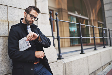 Hes on urban time. a stylish young businessman checking the time while out in the city.の写真素材