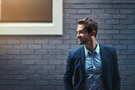 Success waits for no one. a handsome young businessman standing against a grey facebrick wall.の写真素材