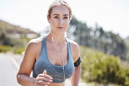 Fitness, woman and running with music for sports exercise, workout or training in nature. Serious, fit and active female runner with headphones listening to audio for exercising or healthy wellnessの写真素材