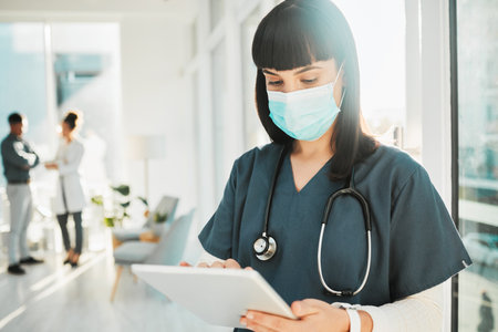Doctor, woman with face mask and tablet, health with digital medical information or research with stethoscope in hospital. Covid, safety and electronic healthcare data with female in ppe and techの写真素材