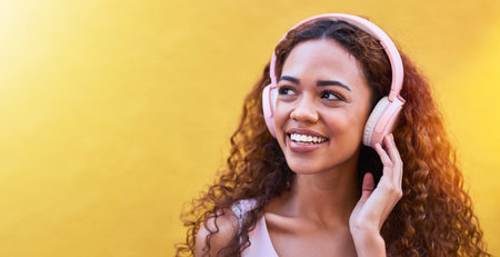 Music, thinking and mockup with a black woman listening to the radio outdoor on a yellow wall background. Headphones, energy and face with an attractive young female streaming audio sound for funの写真素材