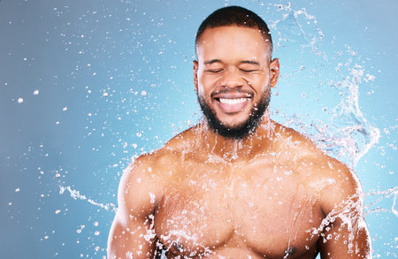 Shower, beauty and water splash for man cleaning, hygiene and skincare isolated in studio blue background. Happy, aqua and model washing smooth skin with glow smile, closed eyes and mockupの写真素材