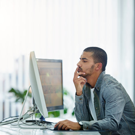 Giving work his undivided attention. a young designer deep in thought while working on a computer in...