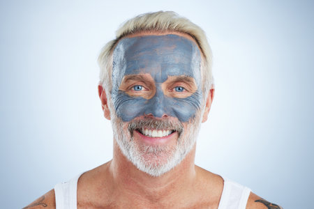 Mask, skincare and facial with portrait of man in studio for cleansing, detox and spa. Cosmetics, beauty and dermatology with senior model on gray background for anti aging, product and naturalの写真素材