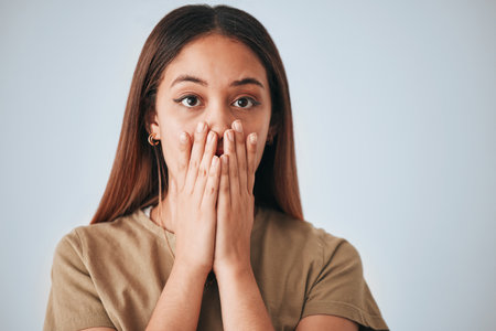 Portrait, woman and surprise in a studio with a female cover mouth from shock. Isolated, grey background and hands on a face of a young person model with wow, worry and alert reaction from secretの写真素材