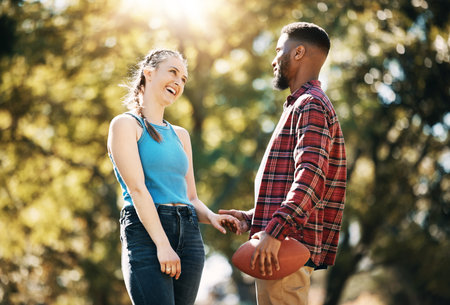 Couple, American football in park and happy together, summer with hand holding outdoor and sports in the sun. Commitment, trust and fitness, black man and woman, interracial relationship and careの写真素材