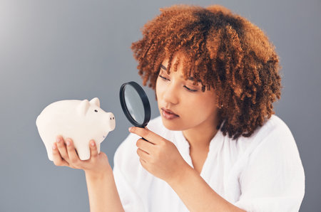 Magnifying glass, piggy bank or black woman with savings budget or financial profits growth on studio background. Curious, cash loan debt or broke girl searching for finances or money investmentの写真素材