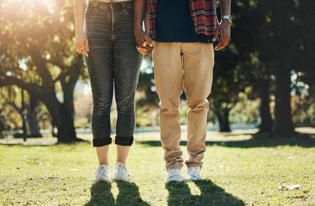 Love, holding hands and shoes of interracial couple in park for calm, freedom or support. Relax, happy and peace with feet of black man and woman standing in grass field for nature, spring or bondingの写真素材